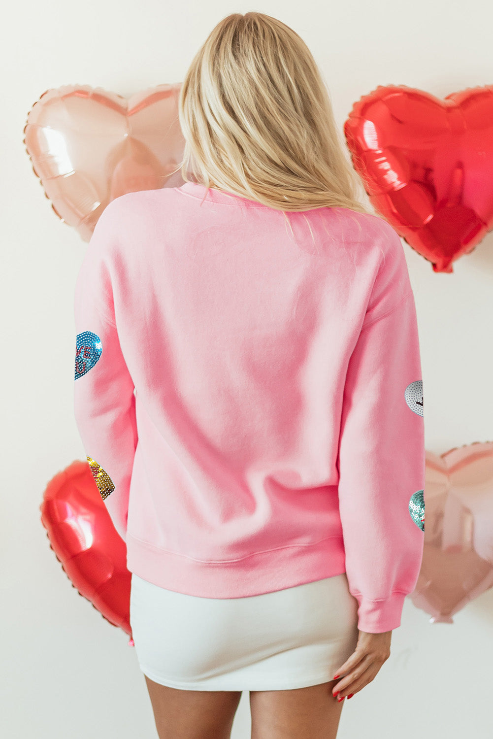 Back view of the Pink Sequin Romantic Letters Heart Graphic Valentines Sweatshirt at Faith & Co. Boutique, showcasing plain pink fabric with sequin heart accents on sleeves.