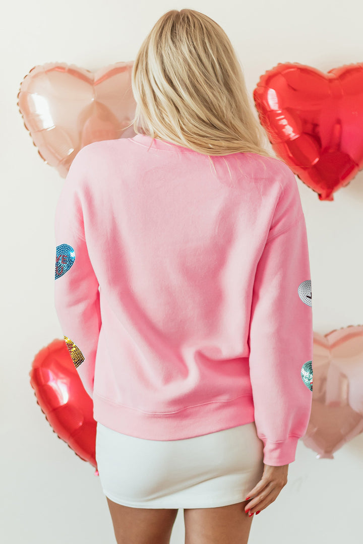 Back view of the Pink Sequin Romantic Letters Heart Graphic Valentines Sweatshirt at Faith & Co. Boutique, showcasing plain pink fabric with sequin heart accents on sleeves.