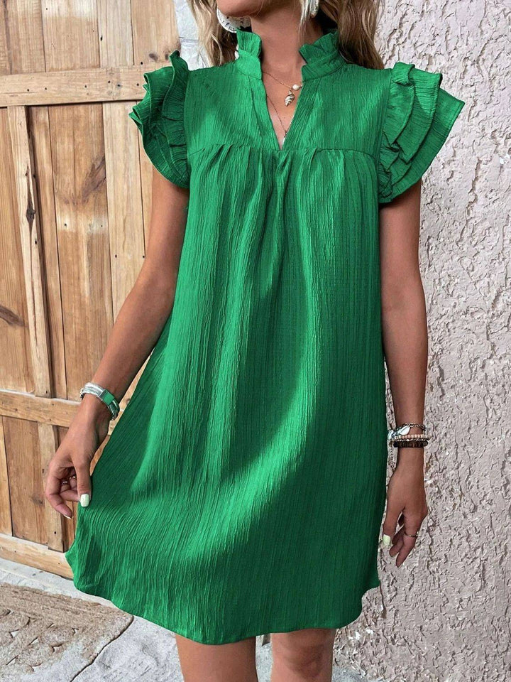 a woman standing in front of a wall wearing a green dress
