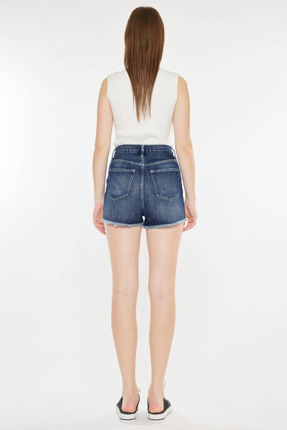 the back of a woman in a white top and denim shorts