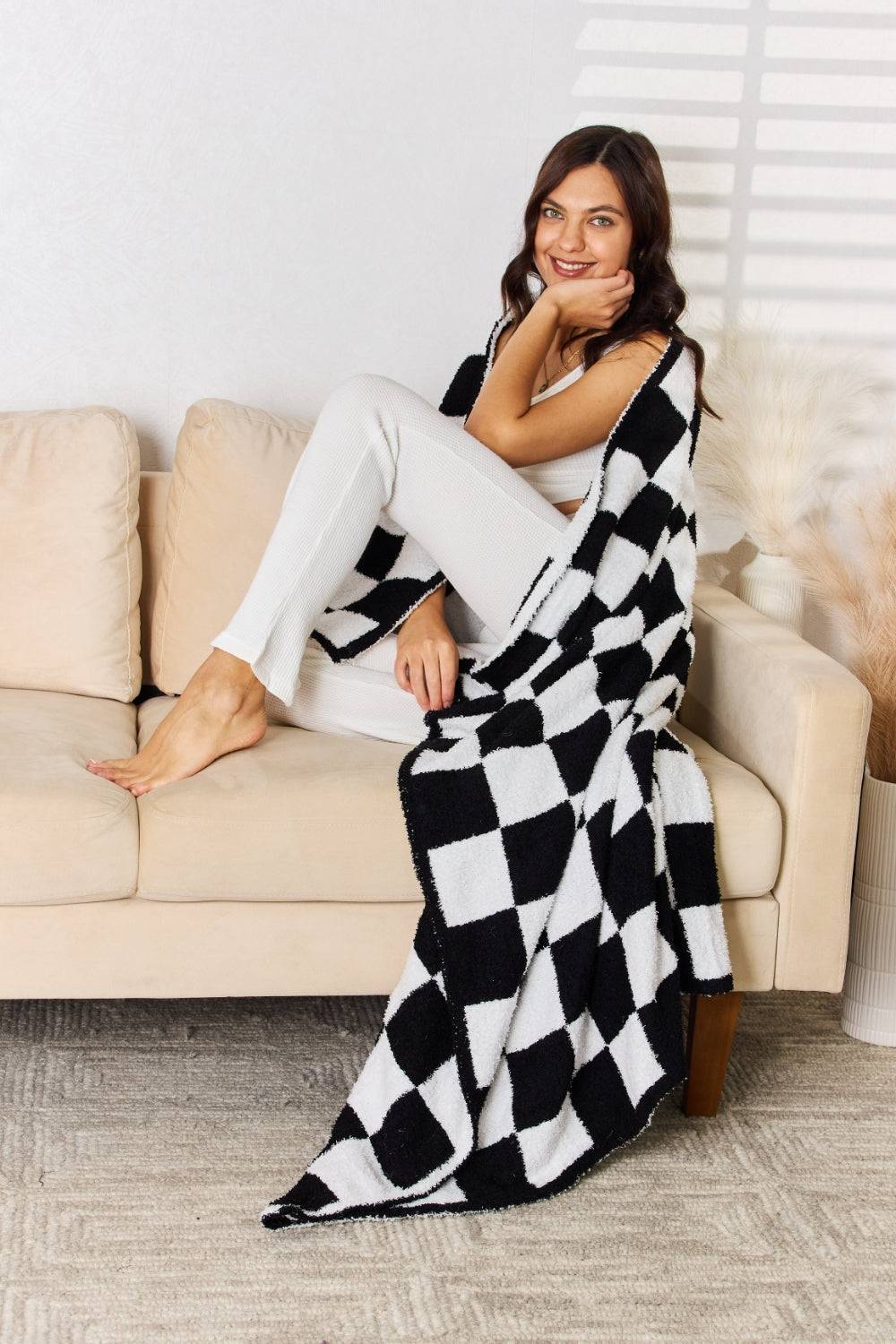 a woman sitting on a couch wearing a black and white blanket