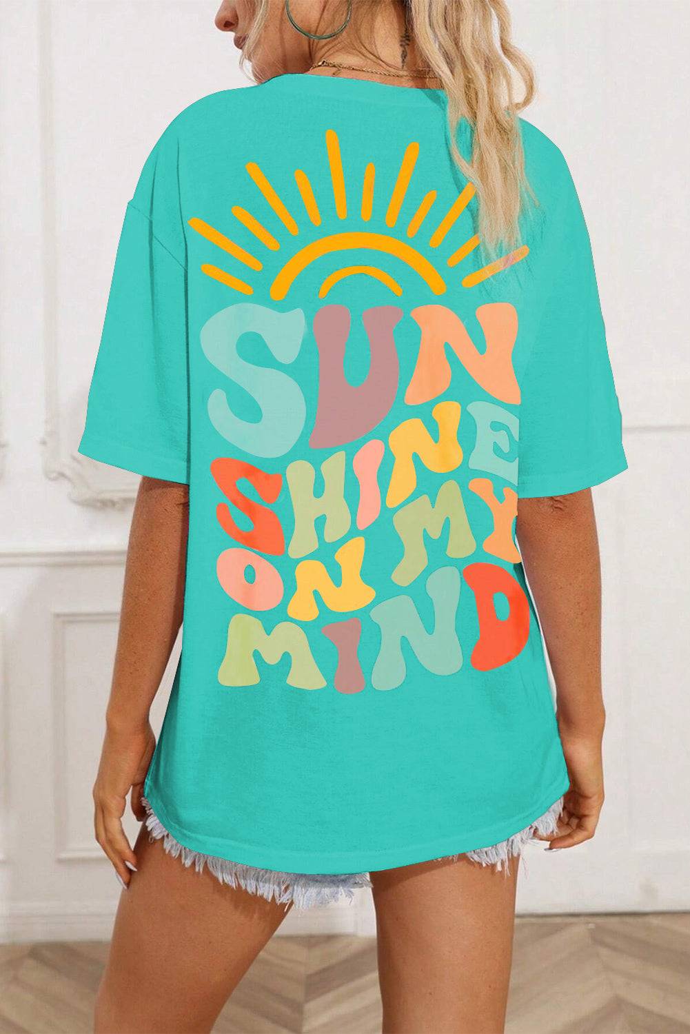 a woman wearing a turquoise shirt with the words sun shine in rainbow on it