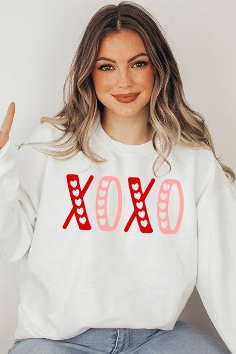 Model wearing Pink & Red XOXO Sweatshirt from Faith & Co. Boutique, a cozy cotton/poly blend with heart print design, perfect for casual wear.