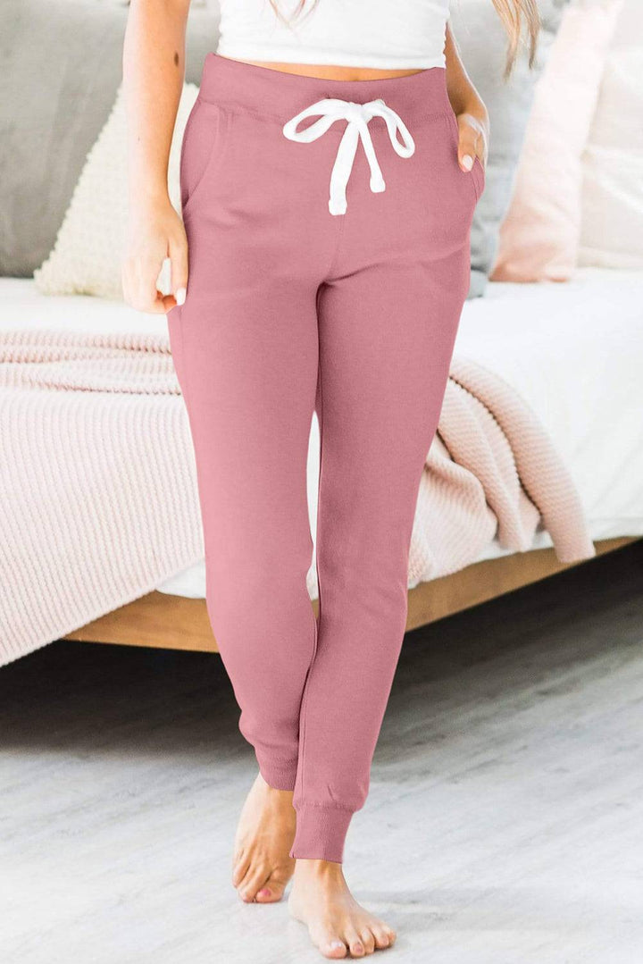 a woman standing in front of a bed wearing pink pants