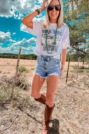 a woman standing in a field wearing a white shirt and denim shorts