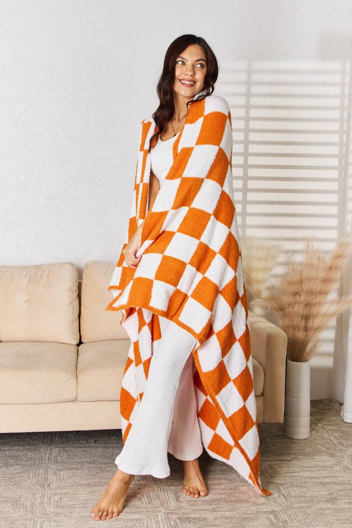 a woman standing in front of a couch wearing an orange and white checkered blanket