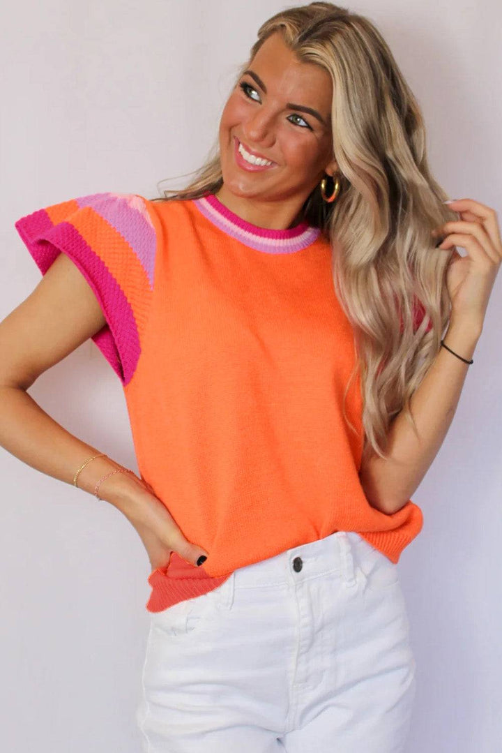 a woman with blonde hair wearing an orange and pink sweater