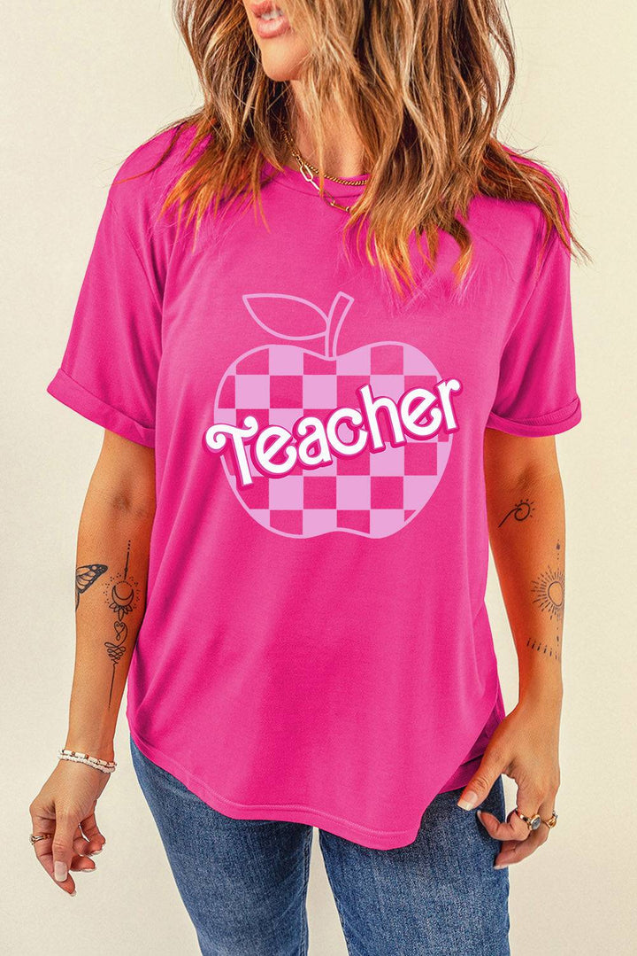 a woman wearing a pink teacher shirt with a checkered apple on it