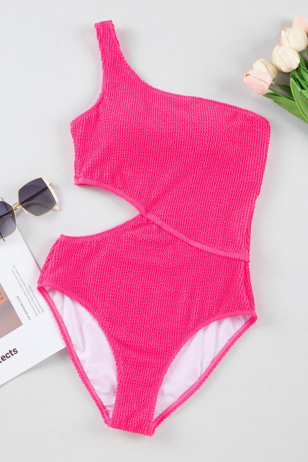 a pink one piece swimsuit next to a pair of sunglasses