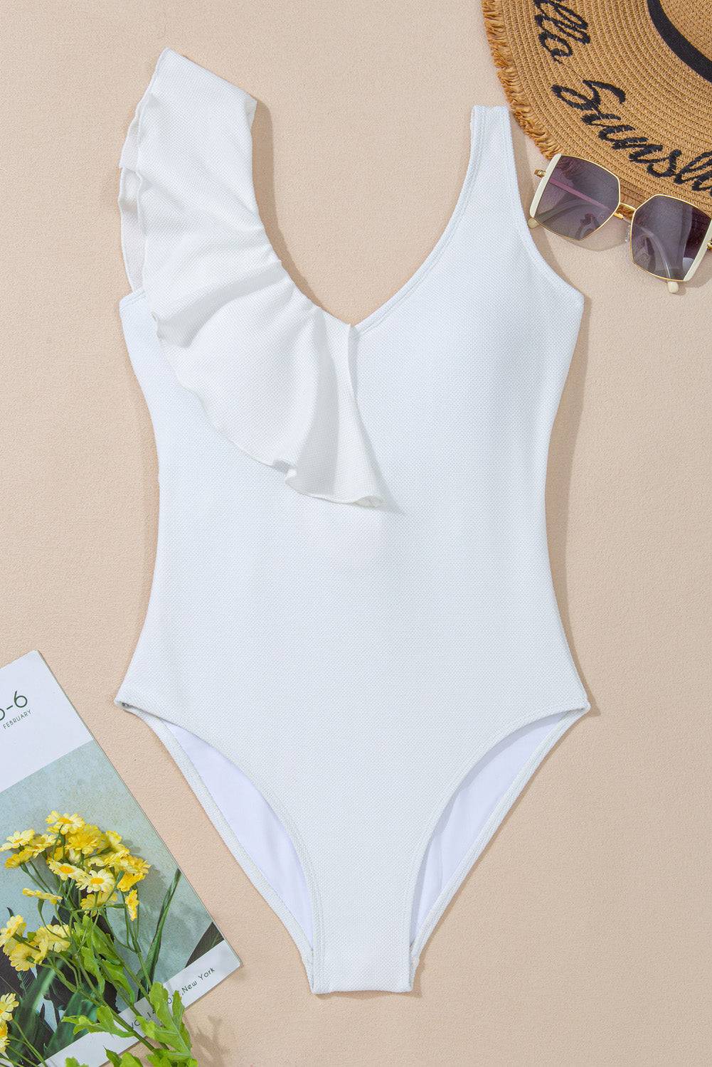 a white one piece swimsuit next to a hat and sunglasses