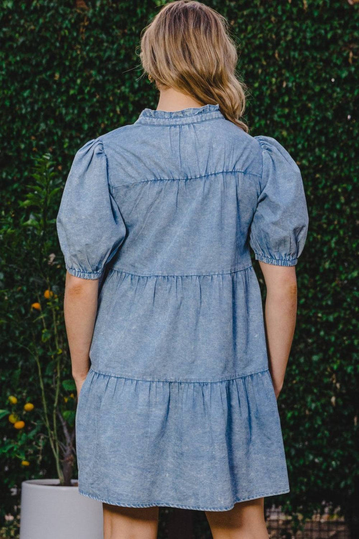 a woman standing in front of a bush wearing a denim dress