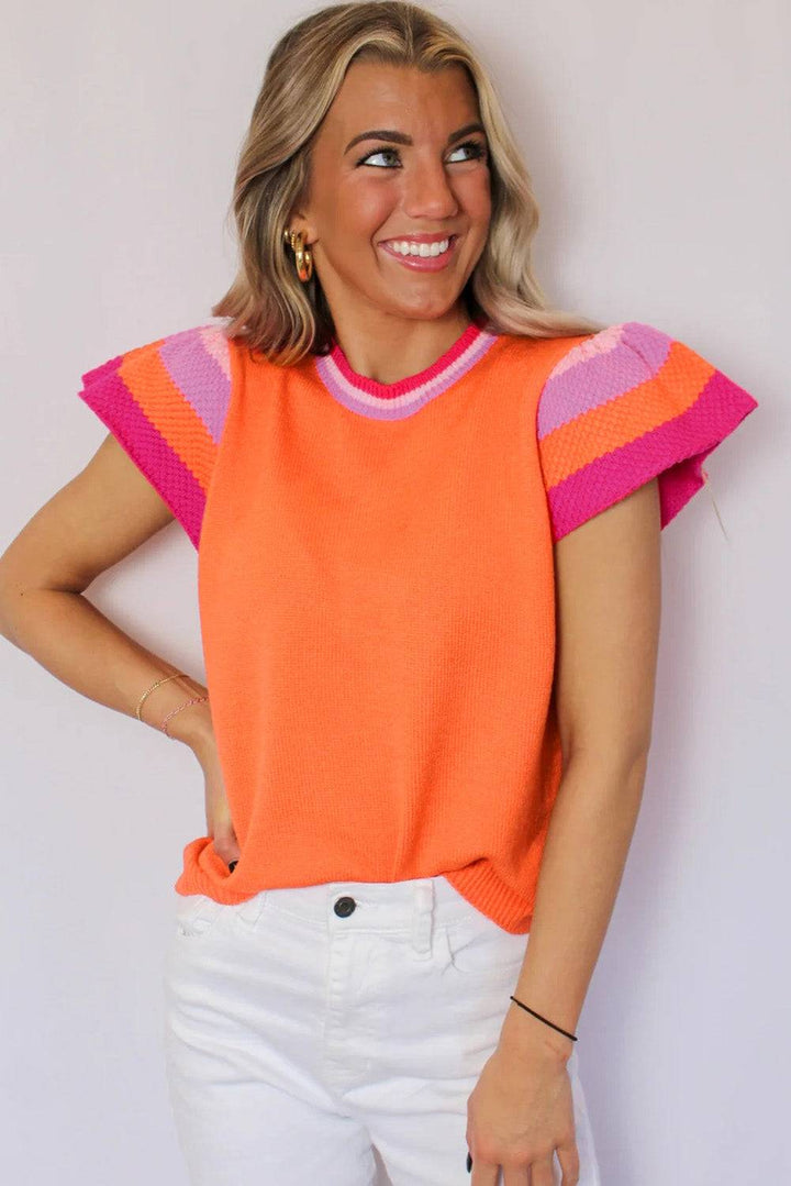 a woman wearing an orange sweater and white pants