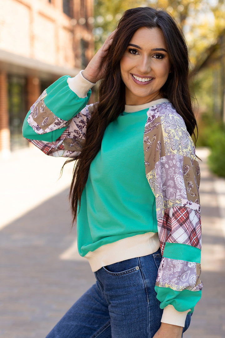 Model posing in Aruba Blue Plaid Vintage Paisley Patchwork Long Sleeve Raglan Top with vibrant patchwork sleeves. Shop now at Faith & Co. Boutique.