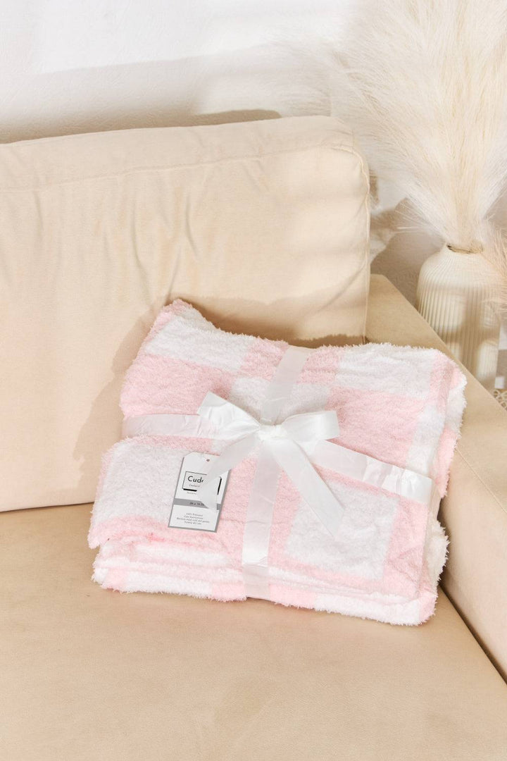 a pink and white blanket sitting on top of a couch