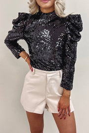 a woman wearing a black sequin top and white shorts