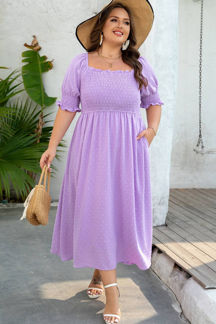Model wearing Wisteria Swiss Dot Smocked Frilled Neckline Plus Size Dress with straw hat and bag, ideal for weddings or summer outings.
