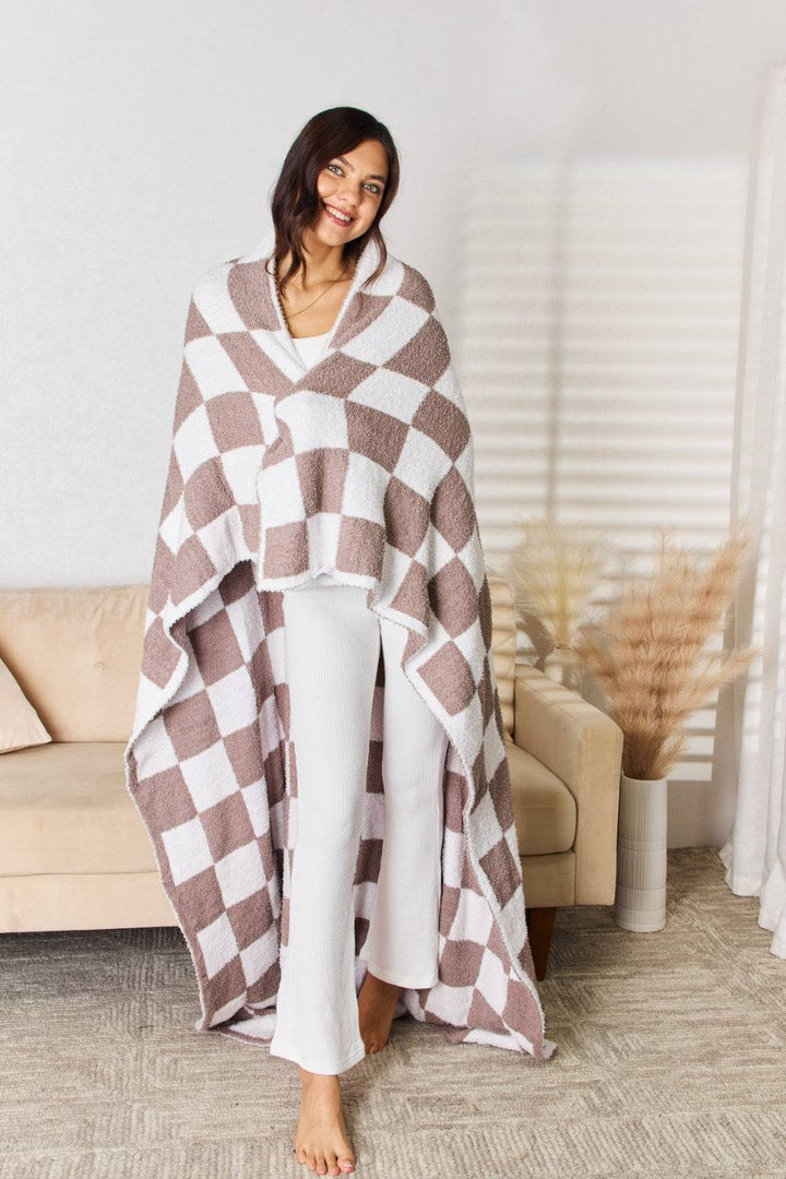 a woman standing in front of a couch wearing a brown and white checkered blanket