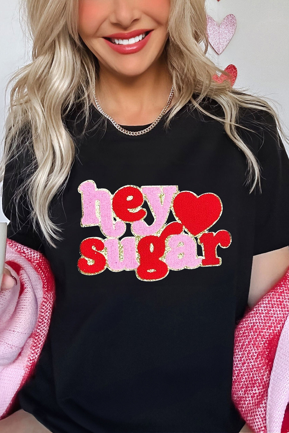 Woman wearing Black Chenille Heart hey sugar Patched Crewneck Valentines Tee, styled with pink accessories for a festive Valentine's Day look.