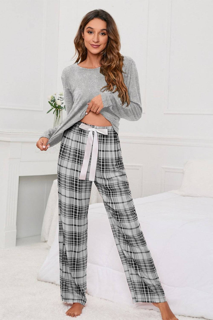 a woman standing on a bed wearing a grey sweater and plaid pants