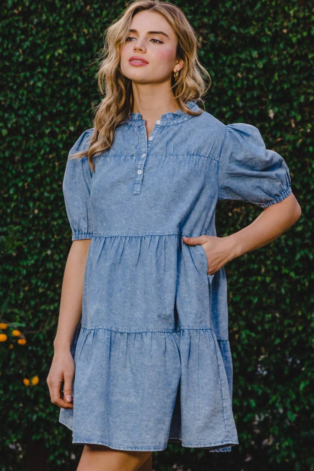 a woman standing in front of a bush wearing a denim dress
