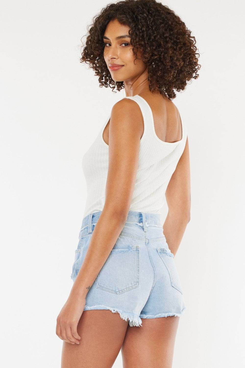 a woman wearing a white tank top and denim shorts