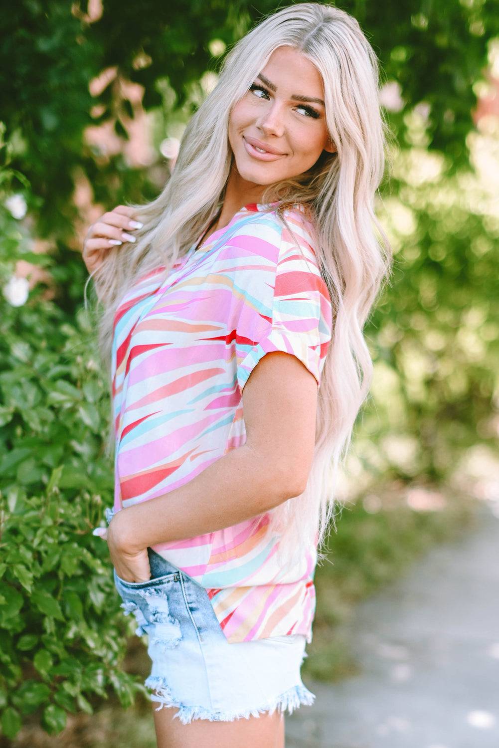 a woman posing for a picture wearing a colorful shirt and denim shorts