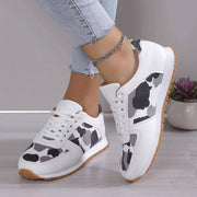a woman wearing white sneakers with black and white cow print