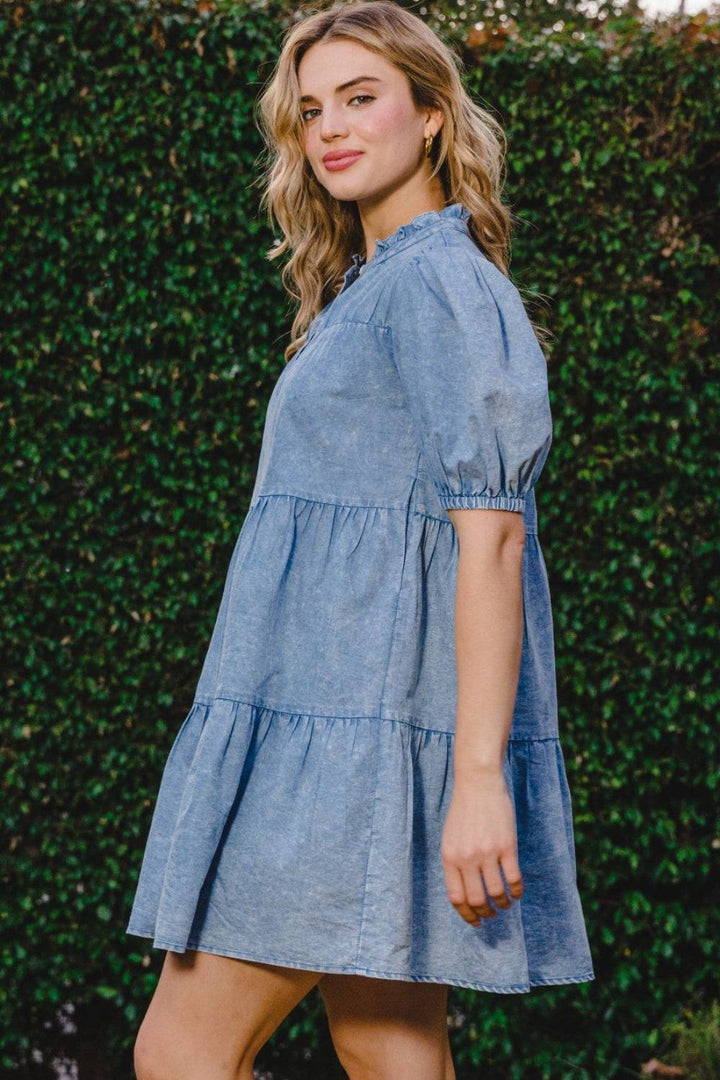 a woman standing in front of a hedge wearing a denim dress
