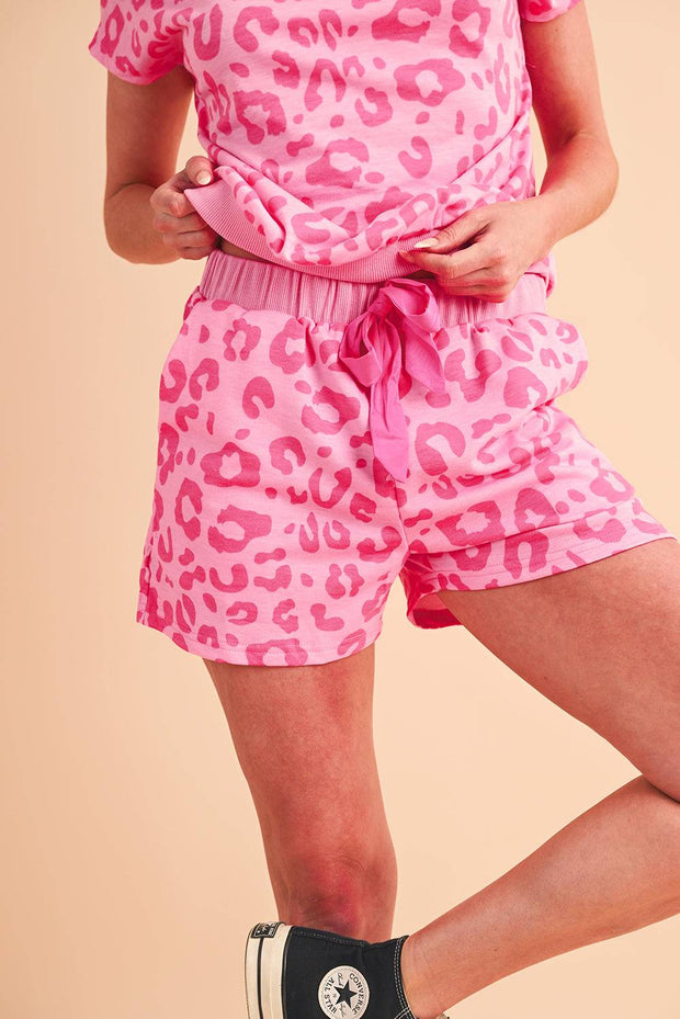 a woman in pink leopard print shorts and black converse sneakers