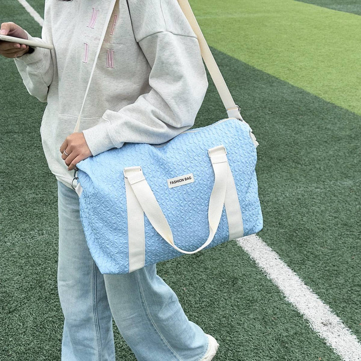 a woman holding a blue duffel bag on top of a field