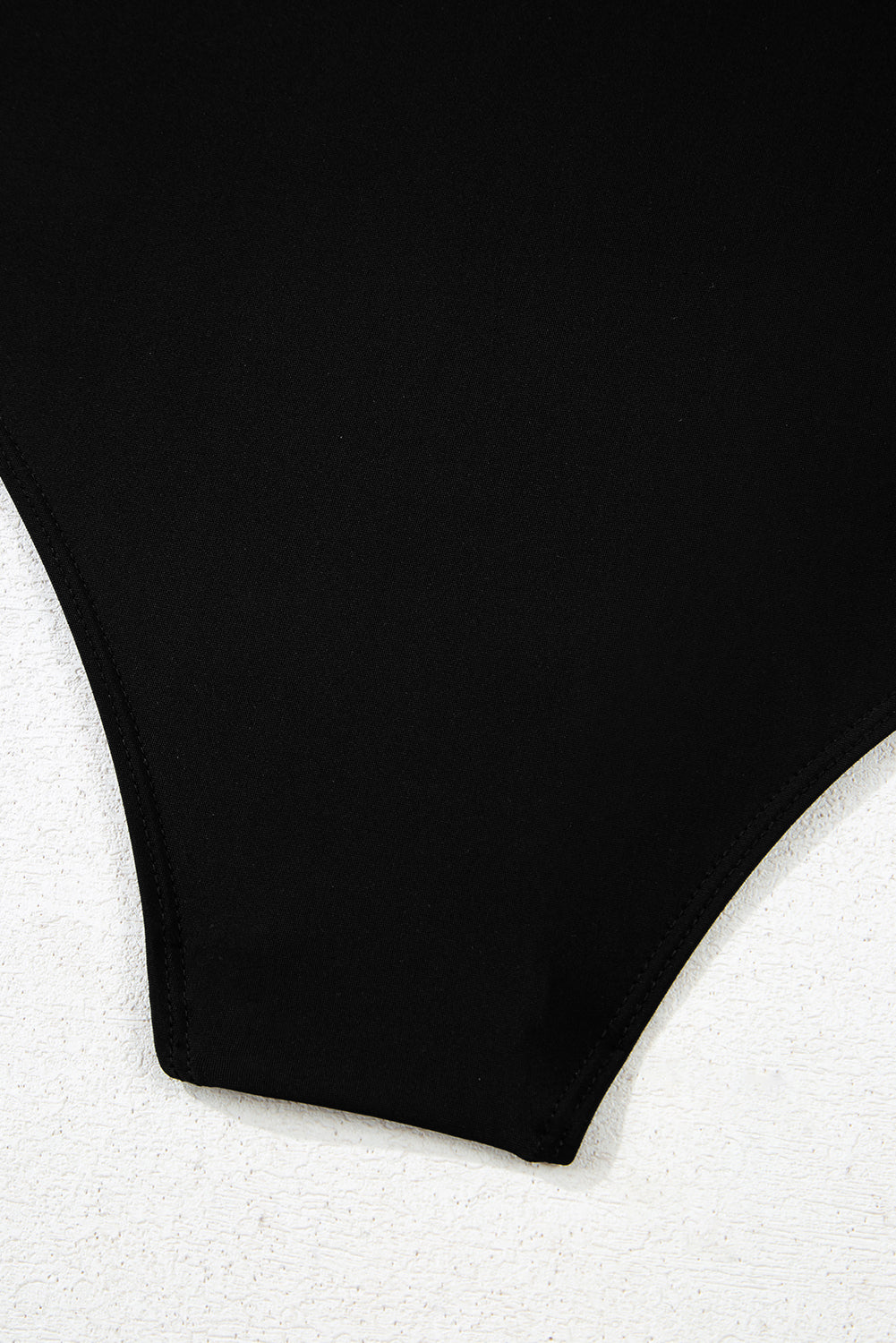 Detailed view of solid black bottom of 2-tone Crossed Cutout Backless Monokini, highlighting smooth fabric and clean stitching.