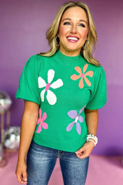 a woman wearing a green sweater with flowers on it