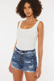 a woman wearing a white tank top and denim shorts