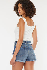 a woman wearing a white tank top and denim shorts
