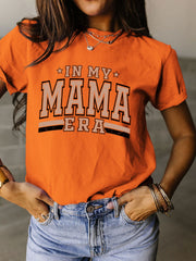 a woman wearing an orange shirt that says in my mama era