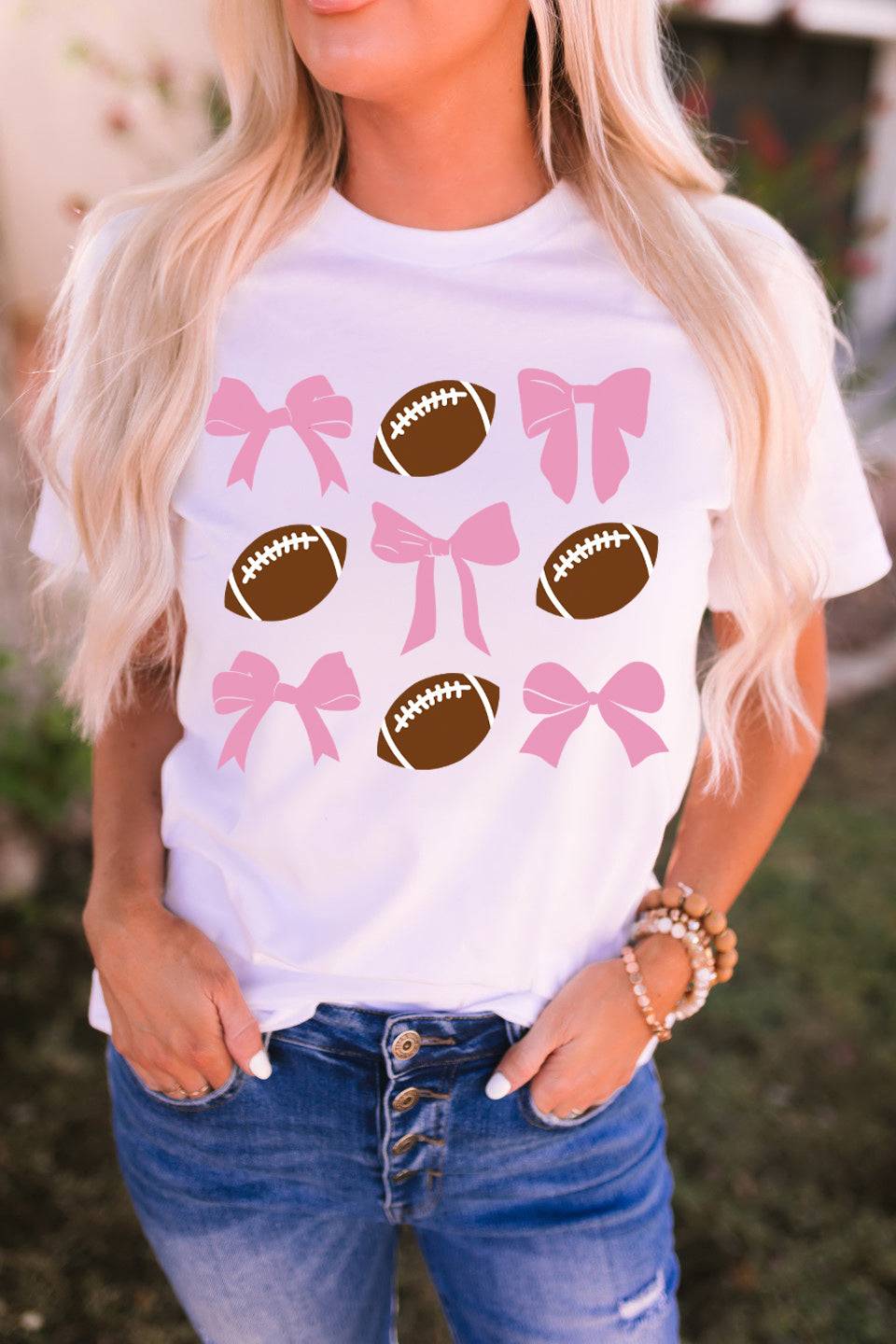 a woman wearing a white shirt with pink bows and footballs on it