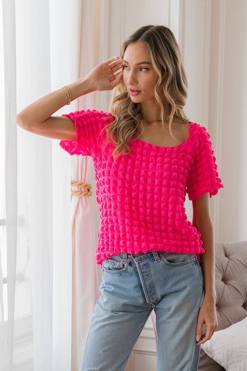 a woman standing in front of a window wearing a pink top