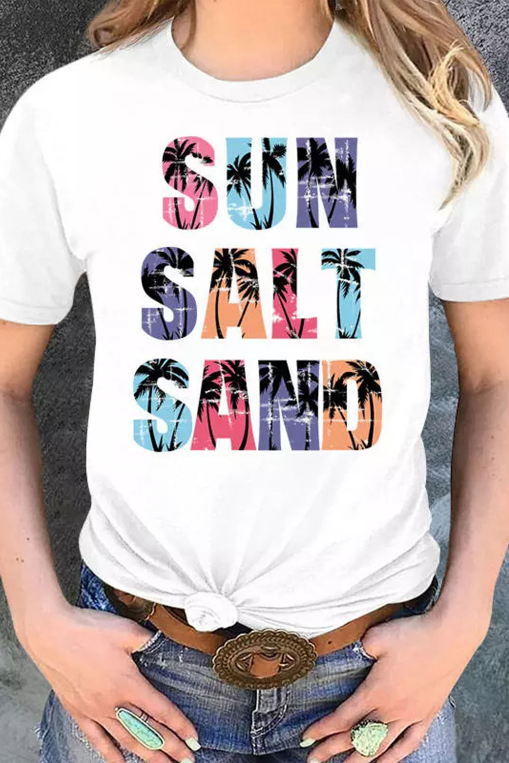 a woman wearing a white shirt with the words sun, salt, sand on it