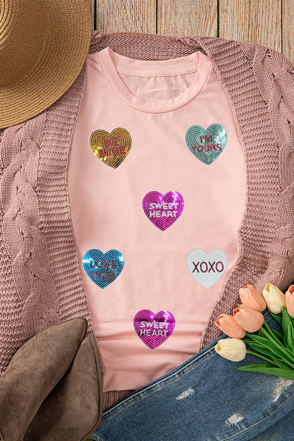 Flat lay of Pink Sequin Valentines Lettering Heart Patched Crewneck T Shirt with sequin heart patches, paired with a knit cardigan and spring accessories. Available at Faith & Co. Boutique.