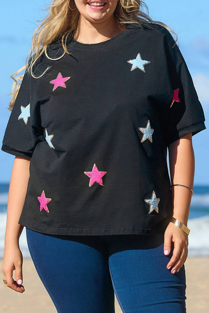 a woman standing on a beach wearing a black shirt with pink and silver stars on