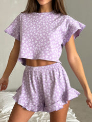 a woman in a purple top and shorts standing on a bed