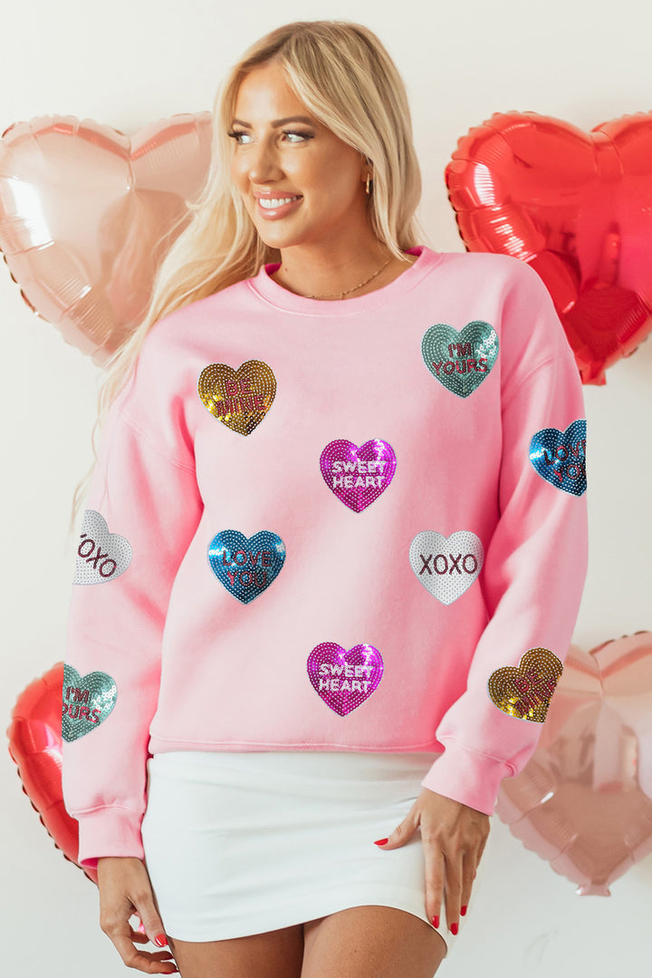 shop Pink Sequin Romantic Letters Heart Graphic Valentines Sweatshirt at Faith & Co. Boutique, featuring colorful sequin hearts with love messages on a pink base. Ideal for Valentine's Day or casual fall wear.