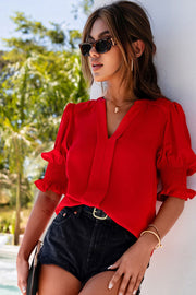 a woman in a red top leaning against a wall