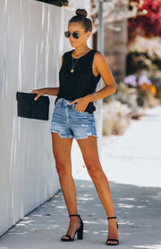 a woman wearing a black top and denim shorts