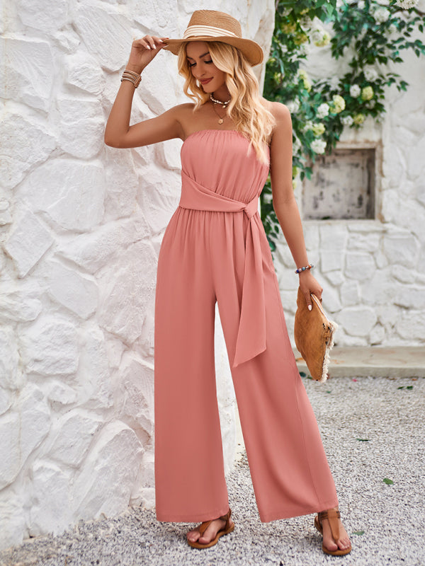 a woman leaning against a wall wearing a pink jumpsuit