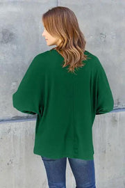 a woman standing against a wall wearing a green sweater
