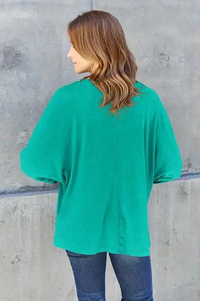 a woman standing against a wall wearing a green sweater