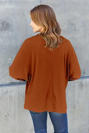 a woman standing against a wall wearing a brown top